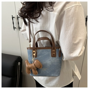 Detail of blue denim crossbody bag with brown leather trim and cute puppy charm accessory