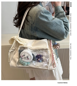 Detail of cream white ita bag featuring a clear window, lace bow and plush accessories