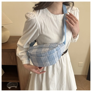 Close-up of a blue and white checkered crossbody chest bag worn with a white dress