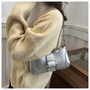 Gros plan d'un sac baguette argenté métallisé avec boucle carrée sur pull jaune