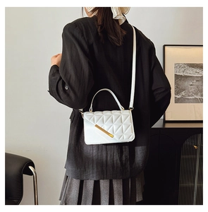 Détail d'un sac bandoulière blanc matelassé avec fermoir doré porté par un mannequin
