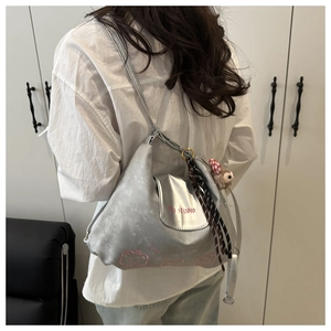 Details der silbernen Metallic-Umhängetasche mit rosa Bärenstickerei und Plüschtier