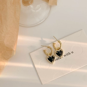 Boucles d'oreilles cœur en or avec pierre noire et cristaux sous une lumière douce