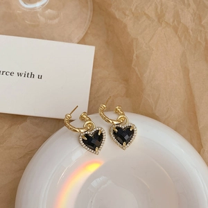 Détail de boucles d'oreilles cœur en or 18K avec pierres noires et oxydes de zirconium