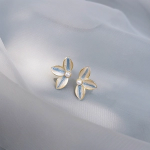 Blue and white enamel flower stud earrings with central pearl on soft fabric background