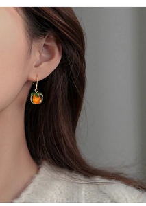 Detail shot of a persimmon-shaped silver earring worn by a model in soft lighting