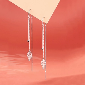 Macro shot of S925 silver leaf tassel earrings with hollow leaf pendant on orange background