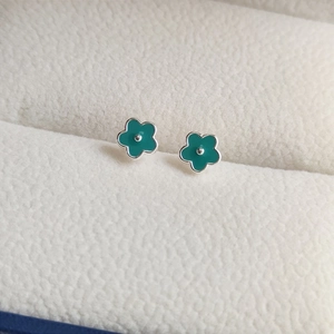 Macro shot of green enamel floral earrings on a cream leather jewelry box interior