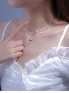 Close-up of double-layer silver necklace with a blue butterfly pendant on a model