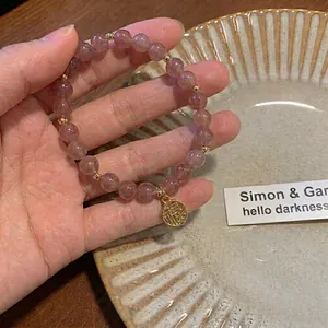 Armband aus rosa Erdbeerquarz-Perlen mit goldenem Glücksanhänger auf Keramikteller