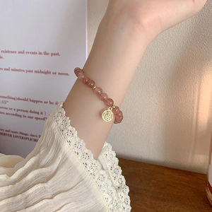 Armband aus rosa Erdbeerkristall mit goldenem Glücksanhänger am Handgelenk