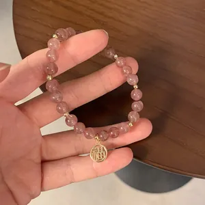 Detailansicht eines Erdbeerkristall-Armbands mit goldenem Fu-Anhänger in Rosa