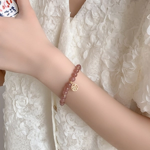 Nahaufnahme eines Erdbeerkristall-Perlenarmbands mit goldenem Anhänger am Handgelenk