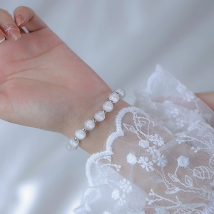 Elegant white cat-eye bead bracelet with silver spacers on a female wrist with lace