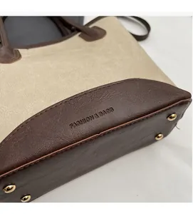 Detail view of tote bag base featuring brown leather stitching and four gold metal feet
