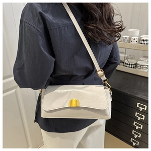 Détail du sac en cuir brillant blanc avec fermoir doré porté à l'épaule sur modèle