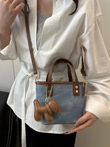 Blaue Denim Mini-Beuteltasche mit braunen Griffen und Welpenanhänger am Modell