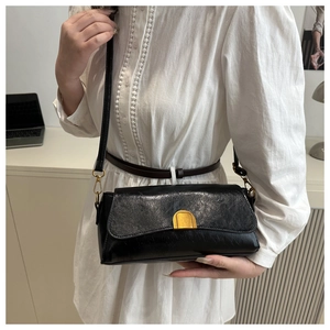 Détail d'un sac bandoulière en cuir noir brillant avec un fermoir doré en demi-lune