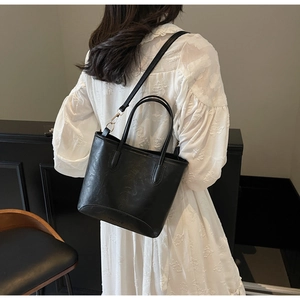 Detail of black PU leather bucket bag with dual straps worn by a model in a white dress