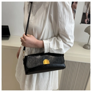 Détail d'un sac baguette vintage noir avec boucle dorée porté à l'épaule