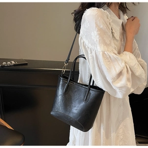 Detail of black tote bag featuring matte wrinkled texture and adjustable metal buckle strap
