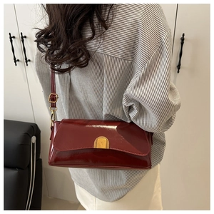 Détail d'un sac baguette en cuir verni bordeaux avec boucle dorée porté par un modèle