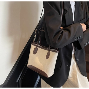 Detailed view of cream canvas bucket bag with brown leather trim shown on model