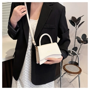 Détail du sac à bandoulière crème avec rabat ondulé asymétrique et boucles dorées