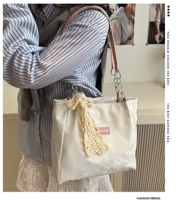 Detail of white tote bag with pink straps and yellow lace bow worn by a model