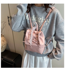Dettaglio mini zaino rosa con bordo in pizzo e fiocco su superficie in pelle lucida