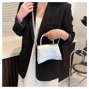 Détail du mini sac argenté avec base ondulée porté par un mannequin en blazer