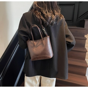 Detail of dark brown leather bucket bag with metallic buckles and adjustable strap