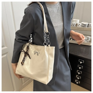 Detail of cream tote bag featuring silver bow logo and chain strap on a model
