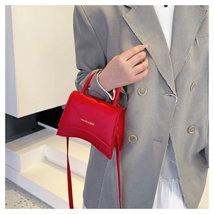 Détail du sac à main en cuir rouge avec base incurvée et logo doré sur costume gris