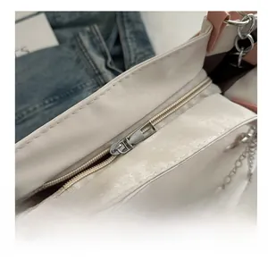 Close-up of a cream tote bag with pink trim, smooth silver zipper and pearl chain detail