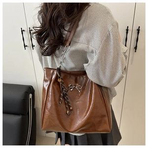 Detail of glossy brown tote bag with metal chain strap and decorative bow charm