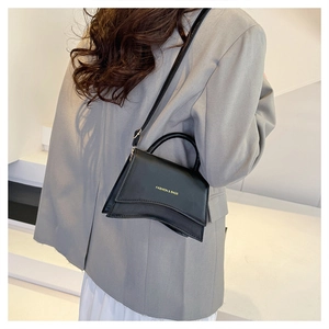 Détail d'un mini sac bandoulière noir avec base incurvée et lettrage doré élégant