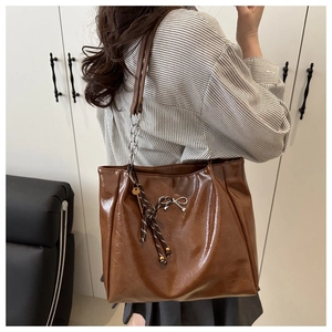 Detail of dark brown tote bag with glossy oil wax leather and silver bow pendant