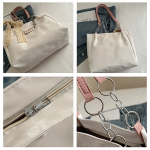 Detailed view of white tote bag showing zipper closure, handle rings and pearl bow charm