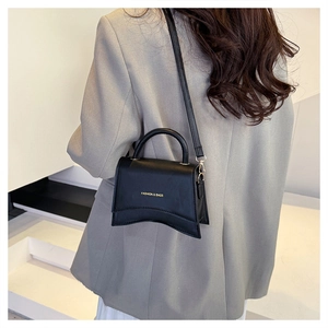 Détail d'un sac à main en cuir noir avec base incurvée porté sur un blazer gris élégant