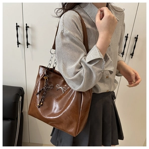 Close-up of brown glossy tote bag with silver chain strap and metal bow pendant detail