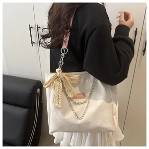 Detail of off-white tote bag with lace bow, pink straps and pearl chain accessories