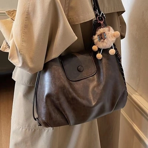 Close-up of deep brown soft leather tote with plush cat charm and striped scarf detail