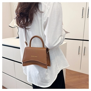 Détail du sac bandoulière marron caramel avec base incurvée et texte doré élégant