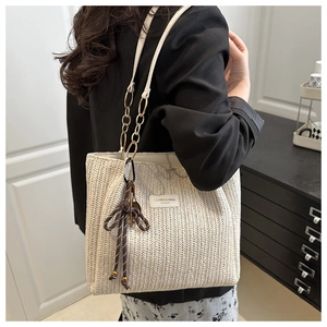 Detail of woven tote bag with leather gold chain handle and decorative bow charm