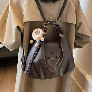 Close-up of a vintage brown leather tote bag featuring a cute alpaca plush keychain