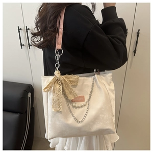 Detail of off-white tote bag with pink leather strap, lace bow, and pearl chain accents