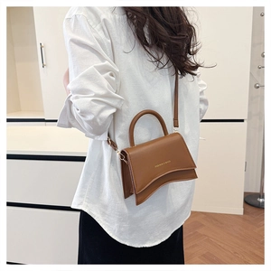 Détail d'un sac bandoulière en cuir marron avec base ondulée et lettrage doré chic