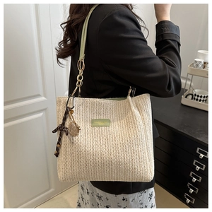 Dettaglio della borsa tote in paglia beige con tracolla in pelle verde e catena oro