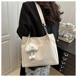 Detail of corduroy tote bag with plush cloud charm and metal chain strap on beige fabric